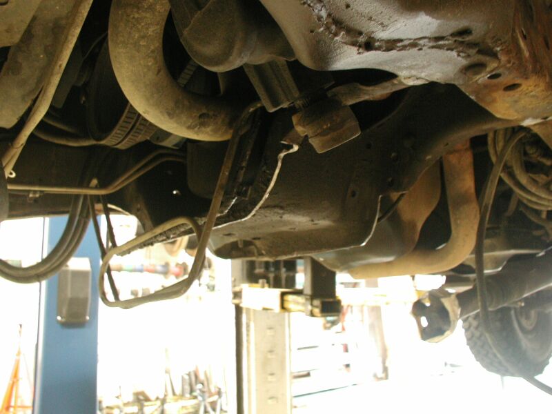 Undercarriage of a lifted vehicle showing axle, springs, and exhaust in a shop