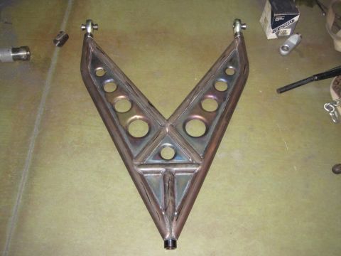 1995 Ford Bronco - A custom-fabricated suspension part with a V-shape and multiple circular cutouts is shown on a workbench.