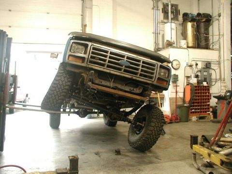 1985 Ford Bronco - This lifted Ford Bronco is undergoing service in a garage, showing its distinctive grille and front end.