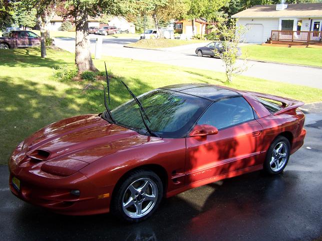 Red 2001 Pontiac Trans Am coupe with black roof parked on wet asphalt