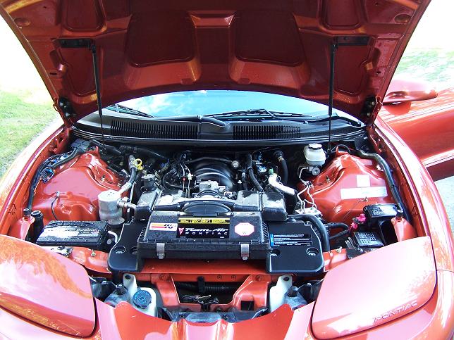 Orange 2001 Pontiac Trans Am engine bay with hood open. Shows engine, battery, and various hoses