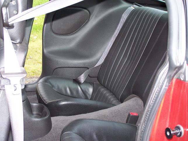 Black leather rear seat and side panel of a red two-door coupe, viewed through the door