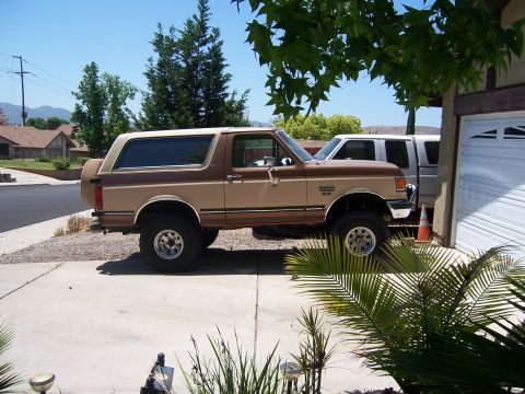1990 Ford Bronco - A two-tone brown 1990 Ford Bronco is parked next to a garage, with another vehicle visible behind it.