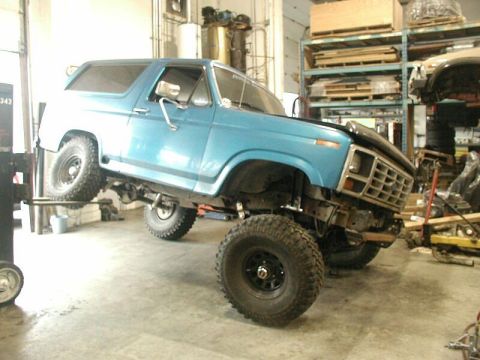 1985 Ford Bronco - Blue Ford Bronco on a lift, undergoing repairs or modifications in a workshop.