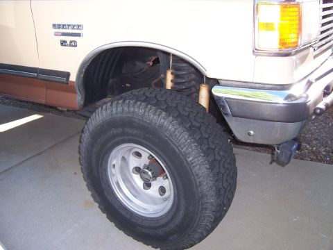 1990 Ford Bronco - Close-up view of the front wheel, fender, and suspension of a Ford Bronco.