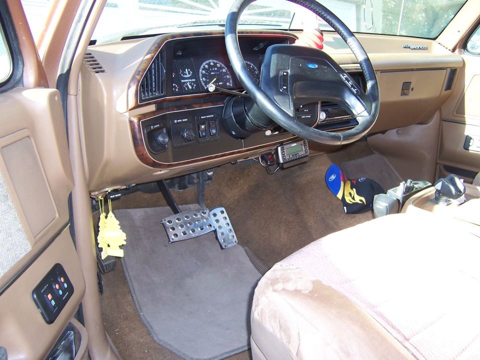 1990 Ford Bronco interior showing dashboard, steering wheel, pedals, and passenger seat