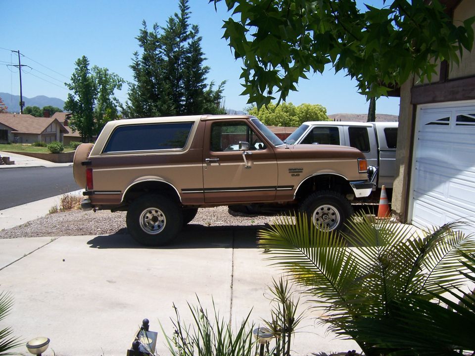 Two-tone tan and brown lifted Ford Bronco SUV, side view, parked in a driveway with big off-road tires