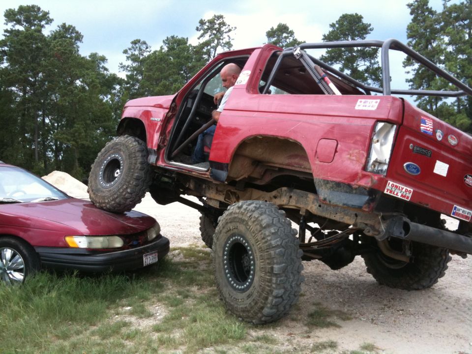 Red Ford Bronco with a roll cage and large tires on top of a maroon sedan