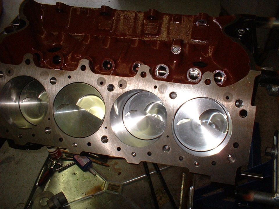 Engine block with pistons visible in cylinders. Top of block is painted dark red