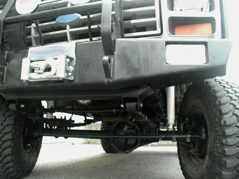 Underside front view of black Ford showing solid front axle, leaf springs, and mud tires