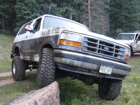 1995 Ford Bronco - 1995 Ford Bronco navigating an off-road obstacle with mud splattered on its body.