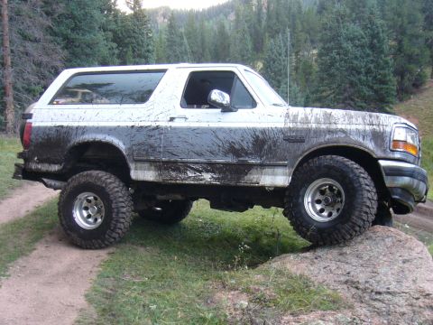 1995 Ford Bronco - This lifted Ford Bronco is navigating a rough, muddy trail with large tires.