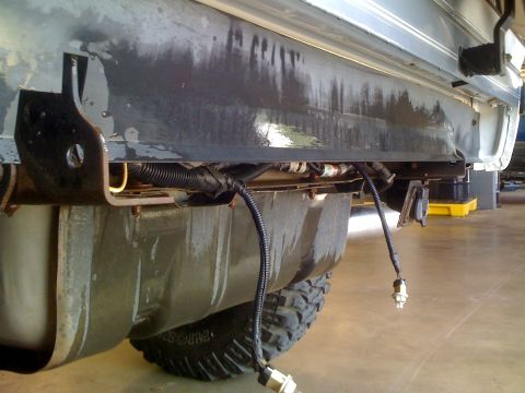 1995 Ford Bronco - Vehicle underbody with fuel tank and exposed wiring harness. Part of a tire is visible.