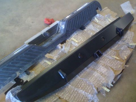 1995 Ford Bronco - Two vehicle bumpers are shown, one with a chrome finish and the other a black steel aftermarket replacement.