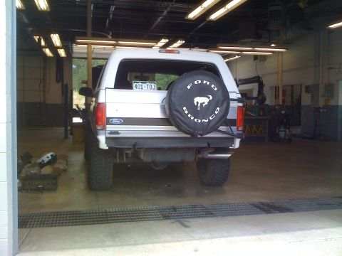 1995 Ford Bronco - Rear view of a white Ford Bronco parked inside a garage with a spare tire mounted on the tailgate.