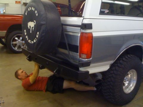 1995 Ford Bronco - A man works on the rear bumper of a 1995 Ford Bronco, which has a spare tire cover with the Bronco logo.