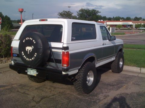 1995 Ford Bronco - This lifted Ford Bronco is parked outdoors, showing its rear end and spare tire cover with the Bronco logo.