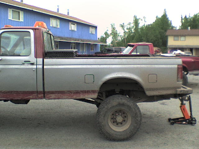 Side view of a 1992 Ford F-series truck with a red cab and silver bed, jacked up at the rear