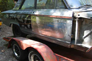 1964 Ford Fairlane - Side view of a car body on a trailer, showing exposed metal and primer.