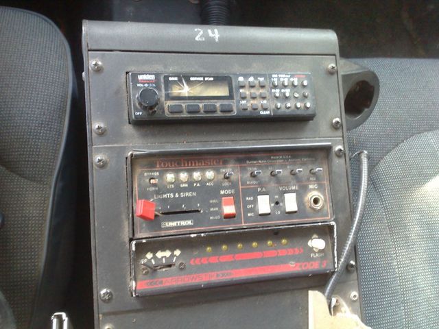 Police car dash with radio, siren controls, and a light bar indicator