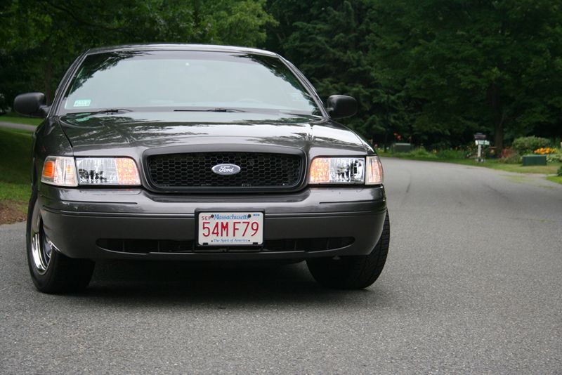 Front view of dark gray Ford Crown Victoria with Massachusetts plate 54MF79 on a tree-lined road