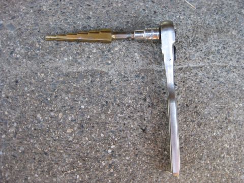 1995 Ford Bronco - A ratchet wrench is connected to a step bit, resting on a concrete surface.