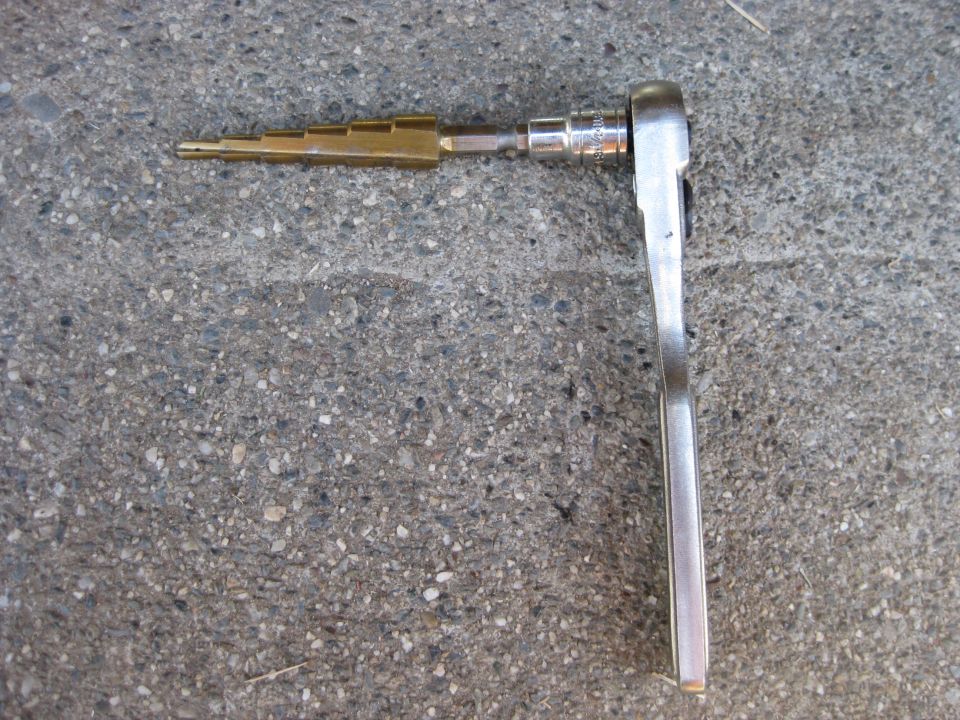 Ratchet wrench attached to a brass step bit on concrete
