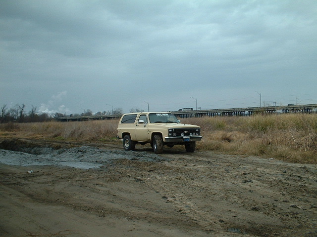 Tan two-door Blazer SUV parked on muddy dirt lot under gray sky