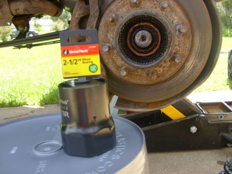 1995 Ford Bronco - A Great Neck wheel bearing package and socket sit beside a vehicle's rusty hub assembly, which is supported by a jack.
