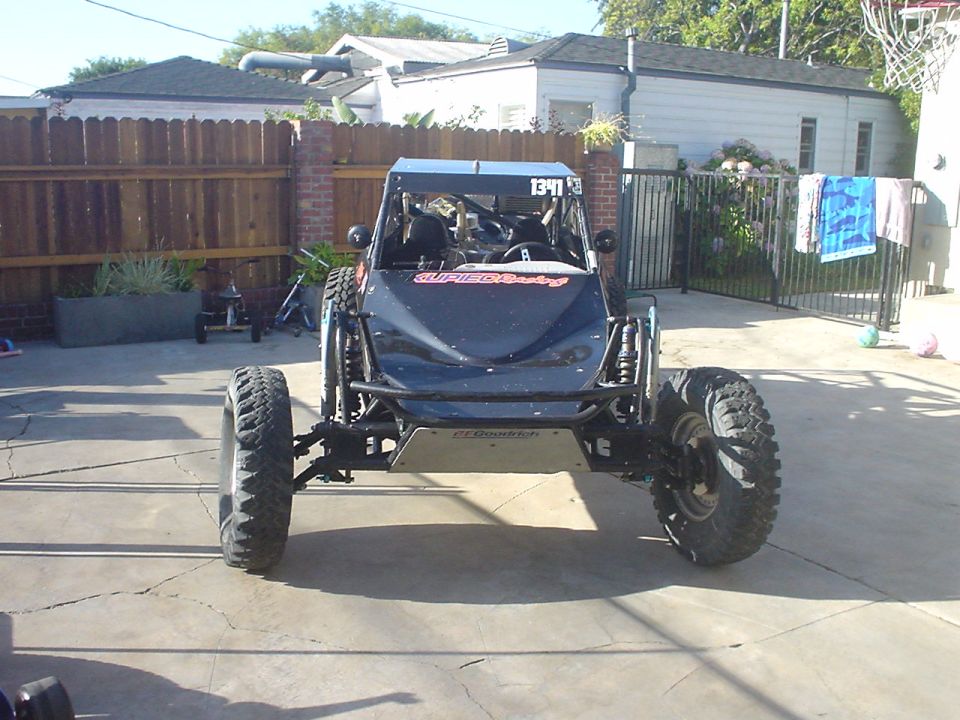 Front view of dark blue tube-frame off-road buggy with long-travel suspension on a driveway