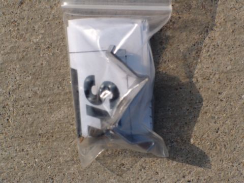1996 Ford Bronco - A plastic bag holds papers with visible numbers and a metal emblem, resting on a concrete surface.