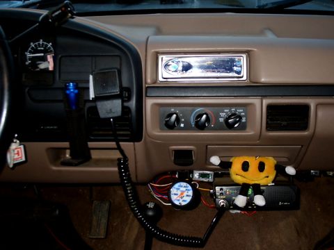 1996 Ford Bronco - The interior of a vehicle shows a CB radio, a gauge, and a plush toy attached to the dashboard.