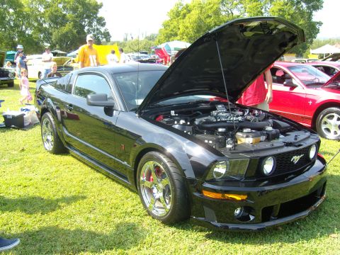 2007 Ford Mustang - A black Ford Mustang is displayed with its hood open at an outdoor car show, with other vehicles visible in the background.