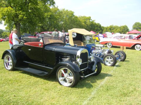 2007 Ford Mustang - Multiple vintage hot rod cars are displayed on a grassy field under a clear sky.