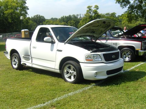 2007 Ford Mustang - A white Ford F-150 SVT Lightning pickup truck is parked on a grassy field with its hood open.