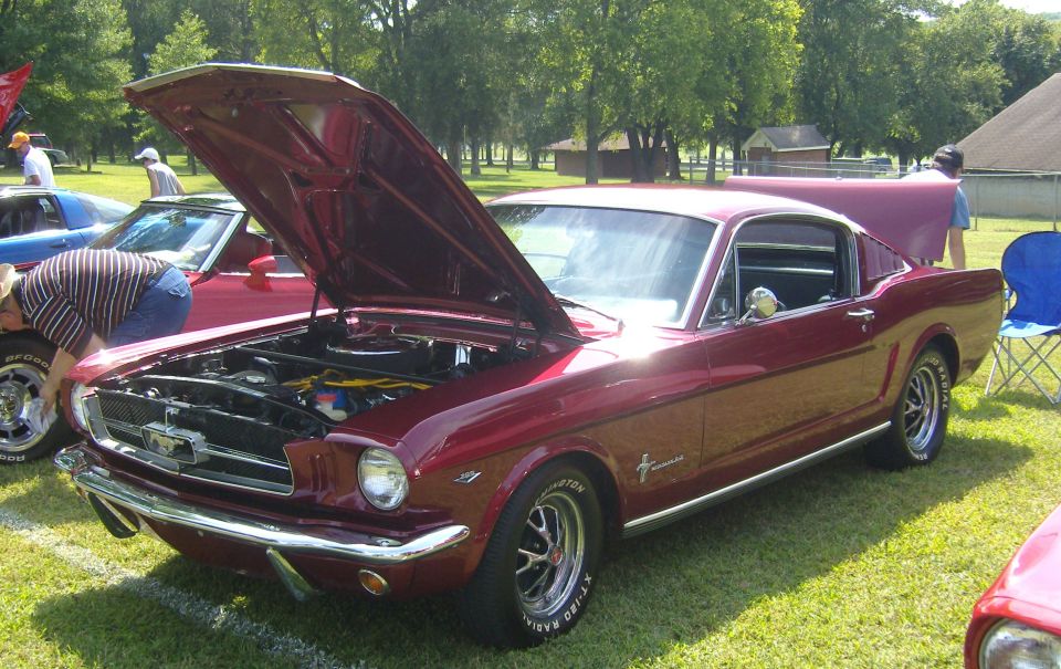 Red 1965 Ford Mustang coupe with hood open, parked on grass