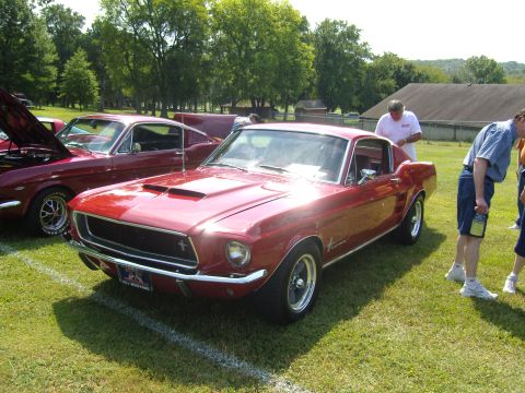2007 Ford Mustang - A red 1967 Ford Mustang coupe is parked on grass next to another Mustang.