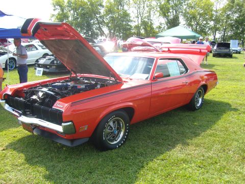 2007 Ford Mustang - A red cougar is parked on a grassy field with its hood open, revealing the engine bay.