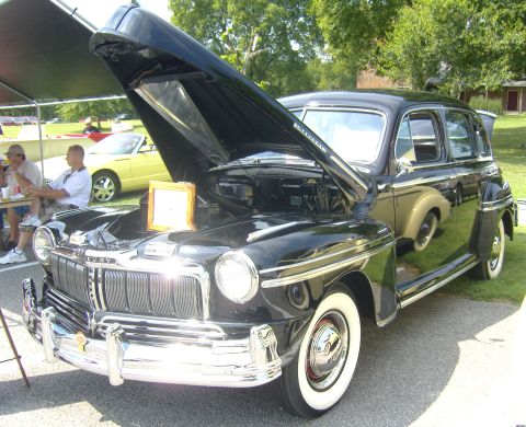 2007 Ford Mustang - This black 1947 Mercury sedan is displayed with its hood open, revealing the engine compartment. A yellow convertible is visible in the bac…