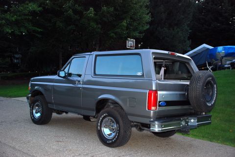 1995 Ford Bronco - This Ford Bronco is parked outside on a paved surface with a grassy area and trees behind it.
