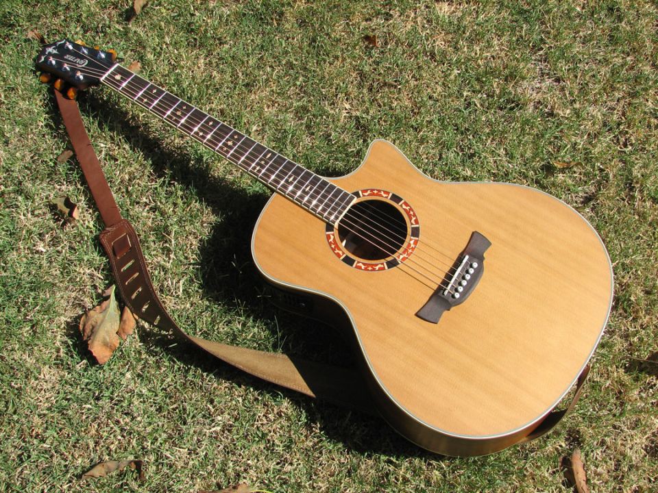 Acoustic guitar with a brown strap lying on grass