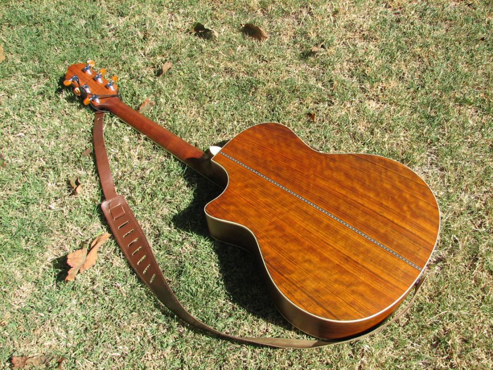 Acoustic guitar with brown strap lying on grass. The guitar has a wooden body and neck