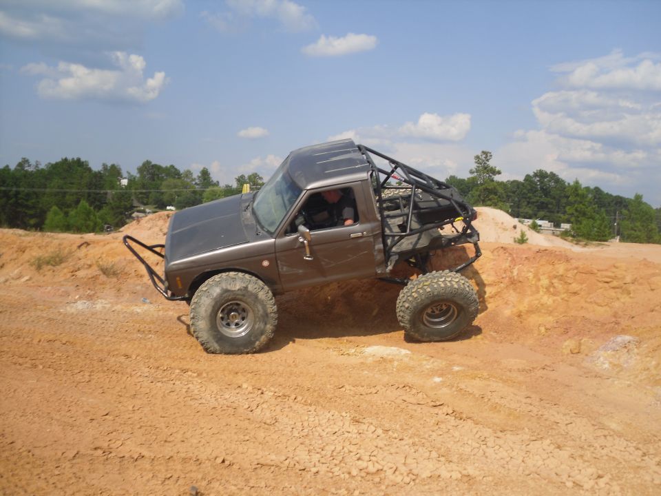 1984 Ford Bronco II with roll cage and large tires climbing a dirt mound