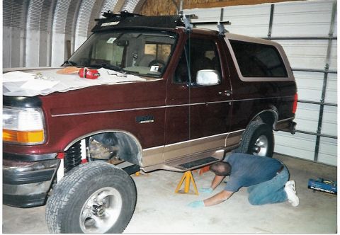 1996 Ford Bronco - A maroon and tan 1996 Ford Bronco is shown with its front end lifted for suspension work.