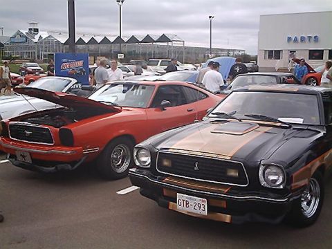 1978 Ford Mustang II - Two Ford Mustang IIs are parked outside a building with a 'PARTS' sign, under a cloudy sky.