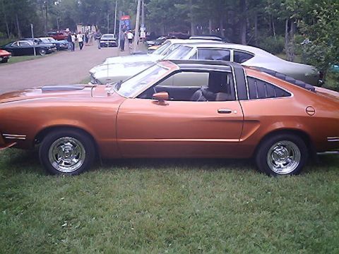 1978 Ford Mustang II - Side view of an orange coupe with a black t-top and louvers on the rear quarter window.