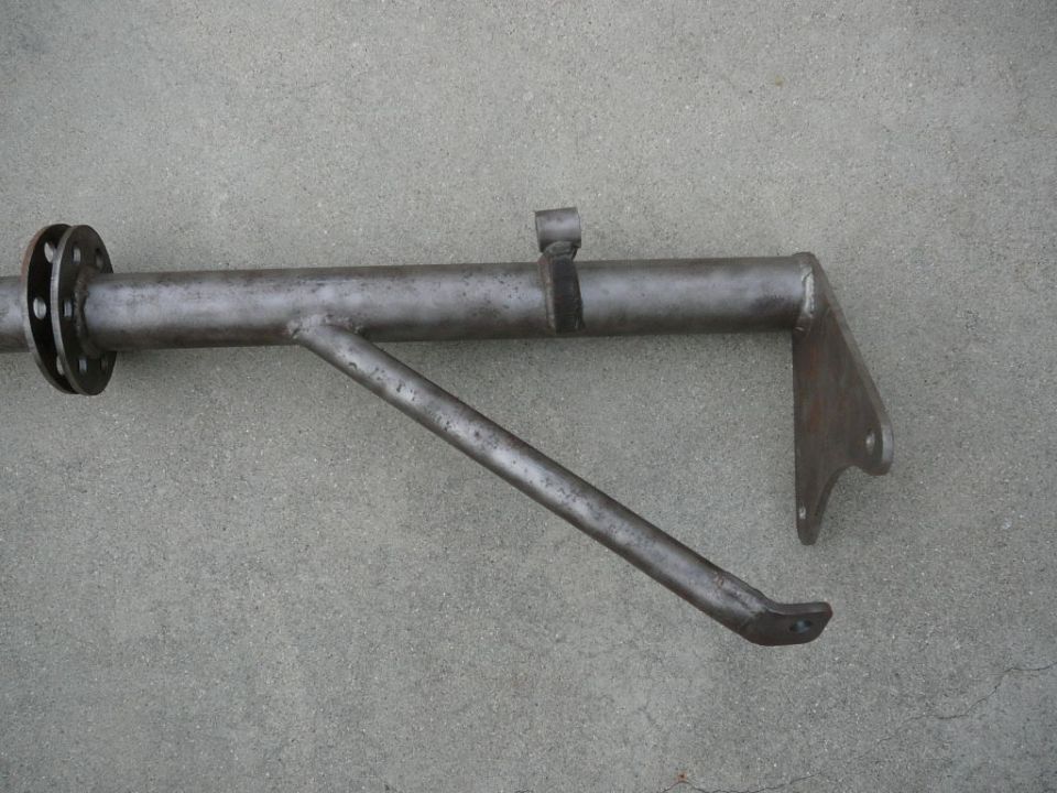 Metal suspension component with a flange on the left and a bracket on the right, resting on a concrete surface