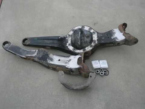 1988 Ford Bronco - Differential axle and control arms with hardware are laid out on a concrete surface.