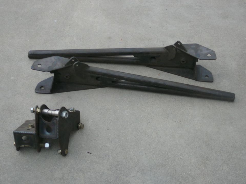 Two dark metal suspension control arms and a small bracket with bolts and a roller
