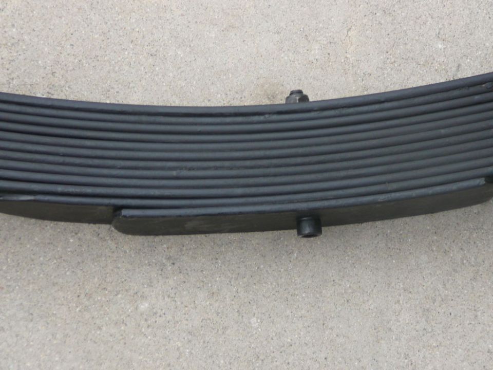 Leaf spring with multiple layers and bolts, resting on concrete